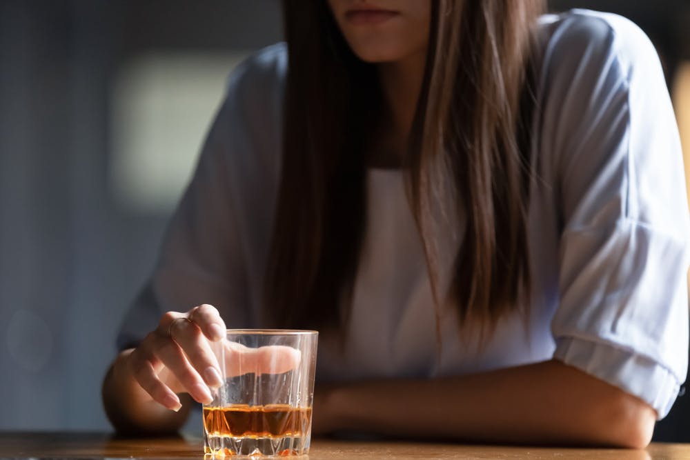 woman sitting with glass of whiskey anxious