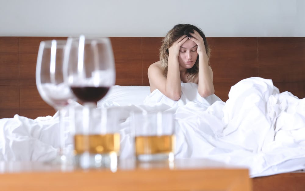 young woman sick in bed with hangover from drinking alcohol